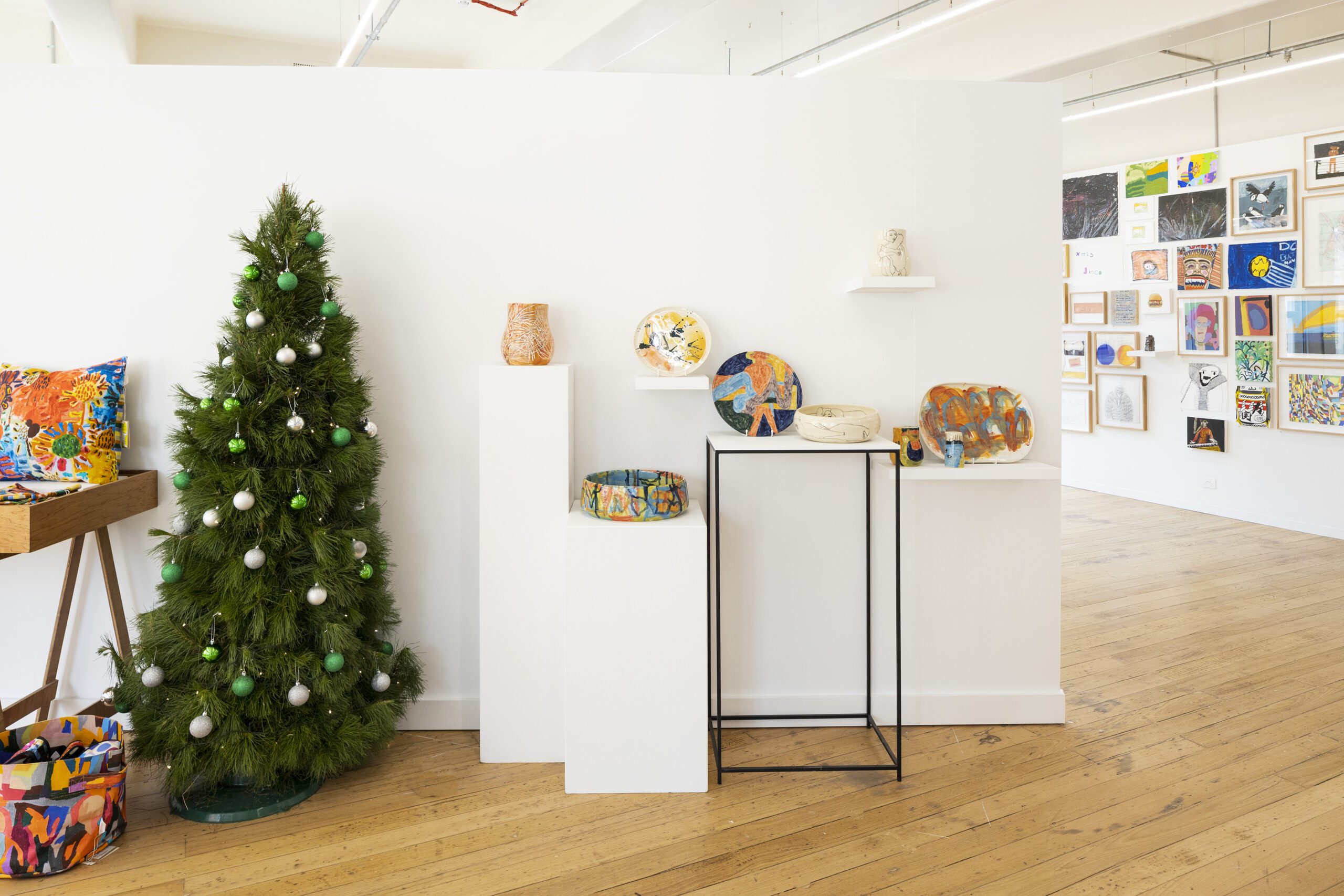 A photo of artworks sitting atop plinths in the APA gallery. On the left hand side is a christmas tree.