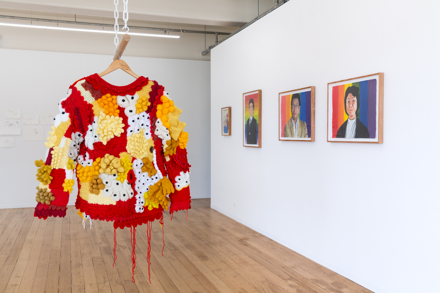 A photo of a red, white and yellow knitted jumper hanging from the gallery roof