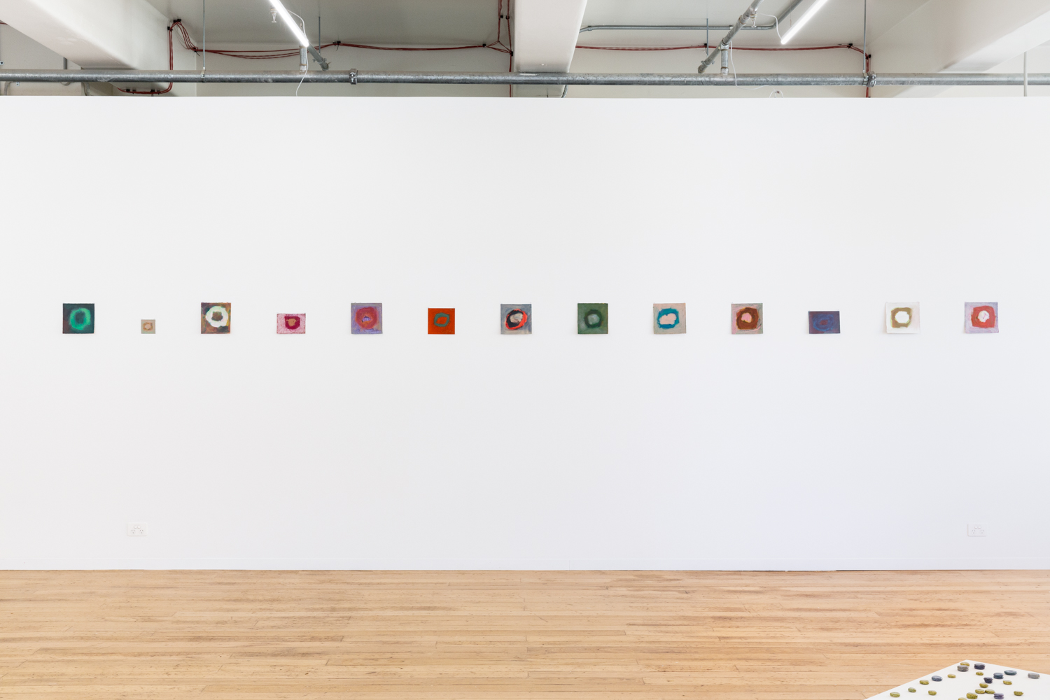 9 square artworks hanging on a gallery wall