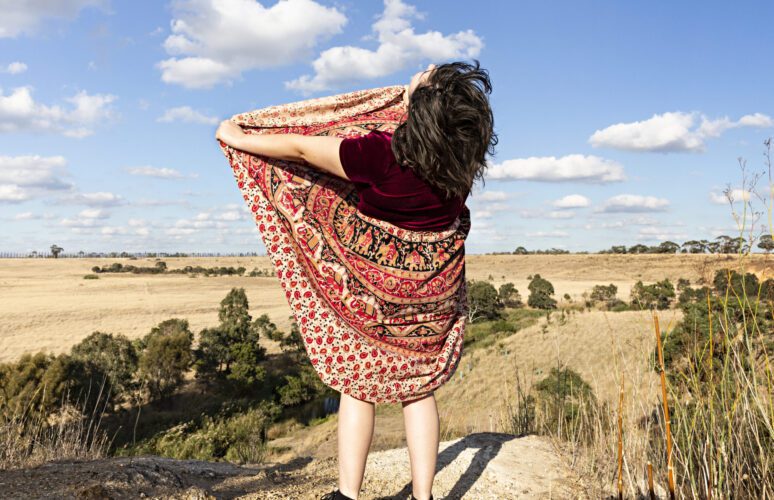 A photo of a person wearing a dress standing above a rock. The person has their back to the camera and is lifting the front of their dress up.