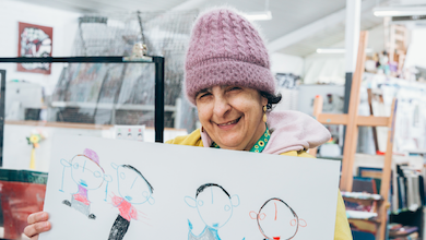 Arts Project Australia artist Nouma Hamra in the Northcote studio holding up one of her artworks.