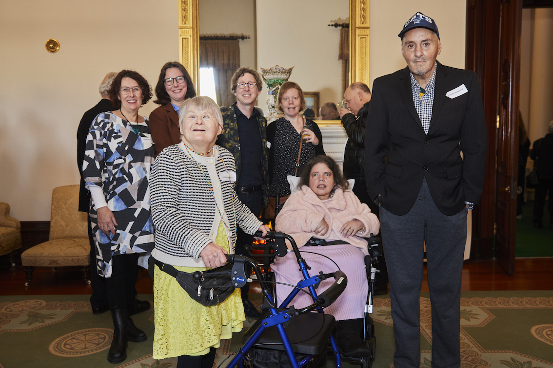 A group of seven people are standing in a line. They are facing the camera and posing for a photo.