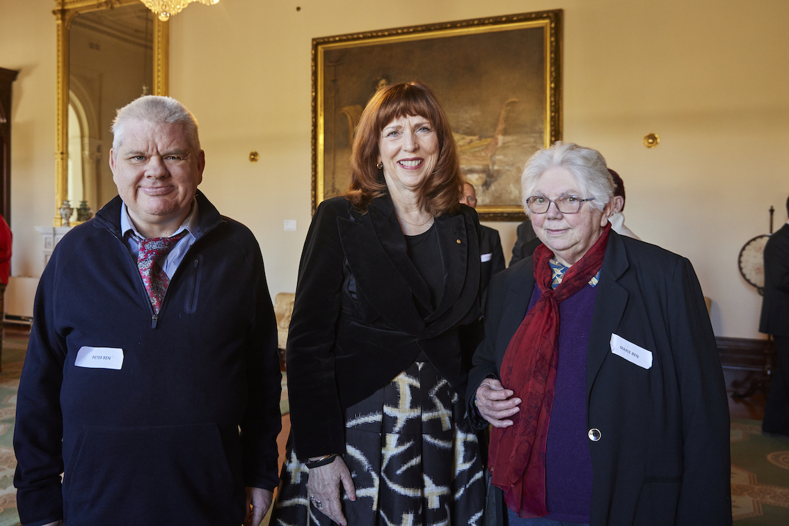A group of three people are standing in a line. They are facing the camera and posing for a photo.