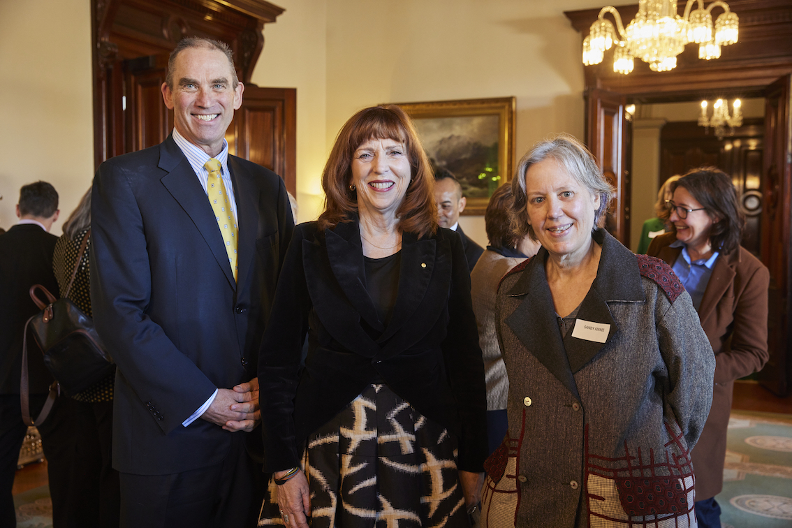 A group of three people are standing in a line. They are facing the camera and posing for a photo.