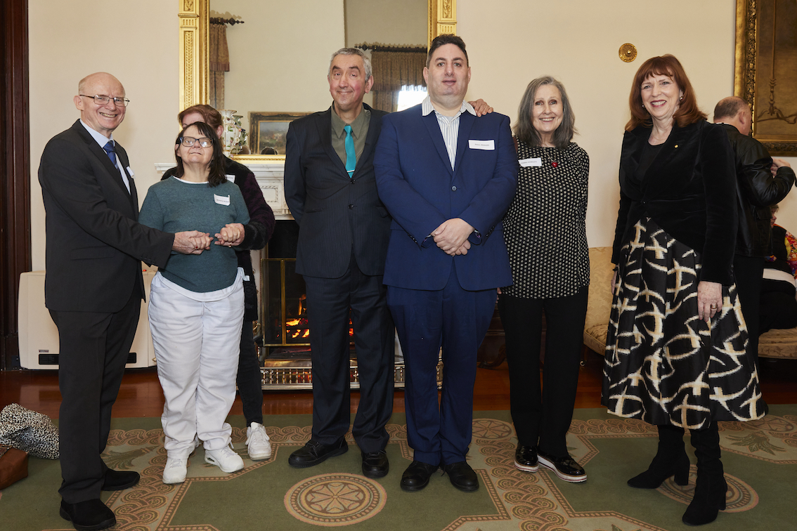 A group of seven people are standing in a line. They are facing the camera and posing for a photo.
