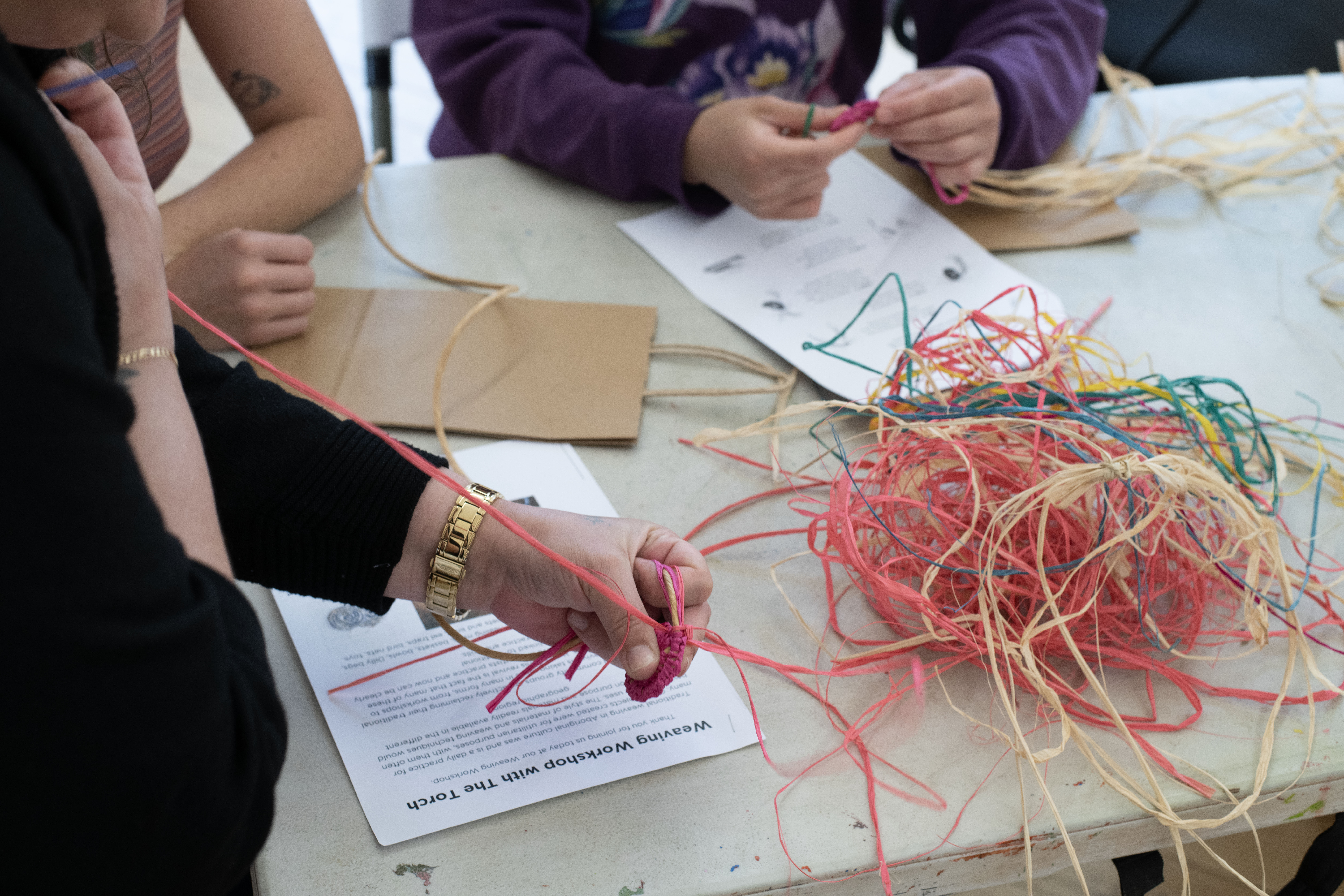 A photo of people holding pink, orange and yellow raffia.