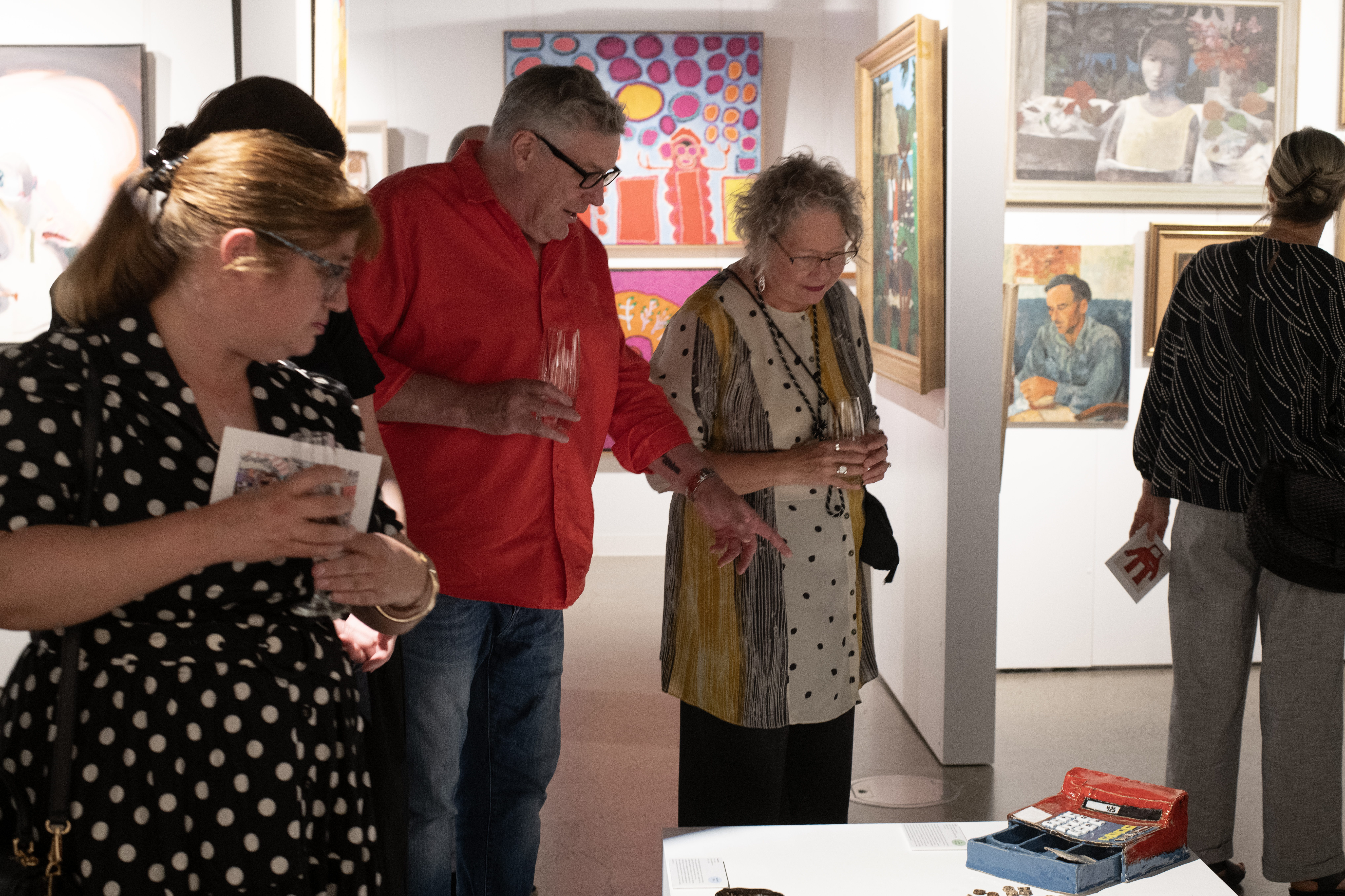 Attendees of the APA fundraiser are crouched over admiring ceramic works by Lisa Reid