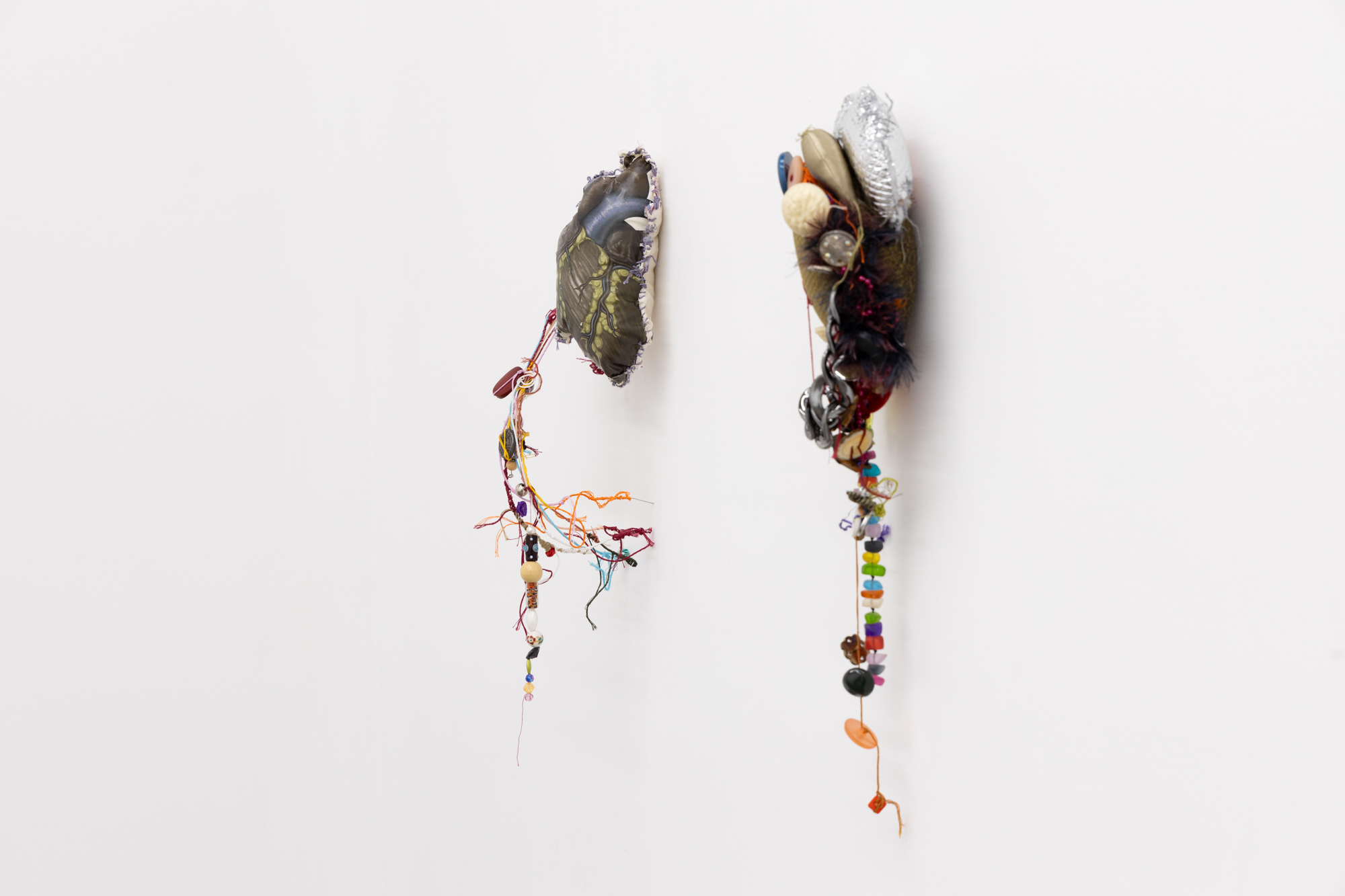 A photo of two soft sculptures made by Bronwyn Hack. The soft sculptures depict a heart and they are made of brightly coloured and textured fabrics with beads and thread woven between the different materials.