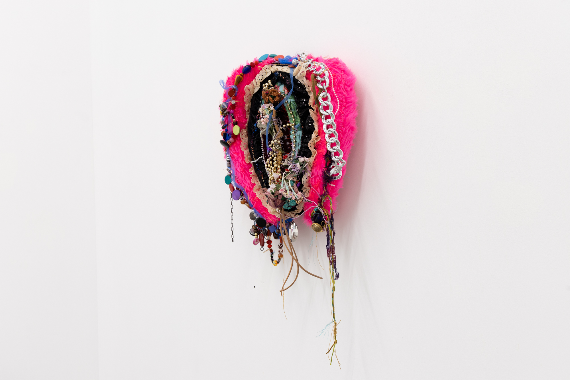 A photo of a soft sculpture made by Bronwyn Hack. The soft sculpture depicts a vagina and is made of brightly coloured and textured fabrics with beads and thread woven between the different materials.