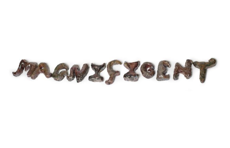 A ceramic work which spells out the word magnificent. It is raku fired giving it a metallic brown and gold finish.